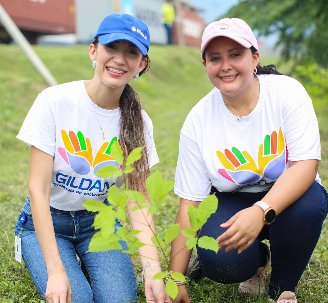 2 employés agenouillés sur l'herbe à côté du jeune arbre qu'ils ont planté ensemble.
