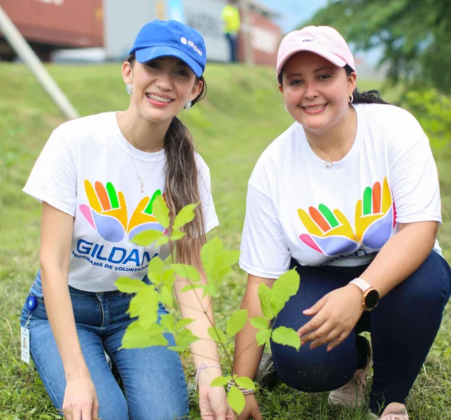 2 employés agenouillés sur l'herbe à côté du jeune arbre qu'ils ont planté ensemble.