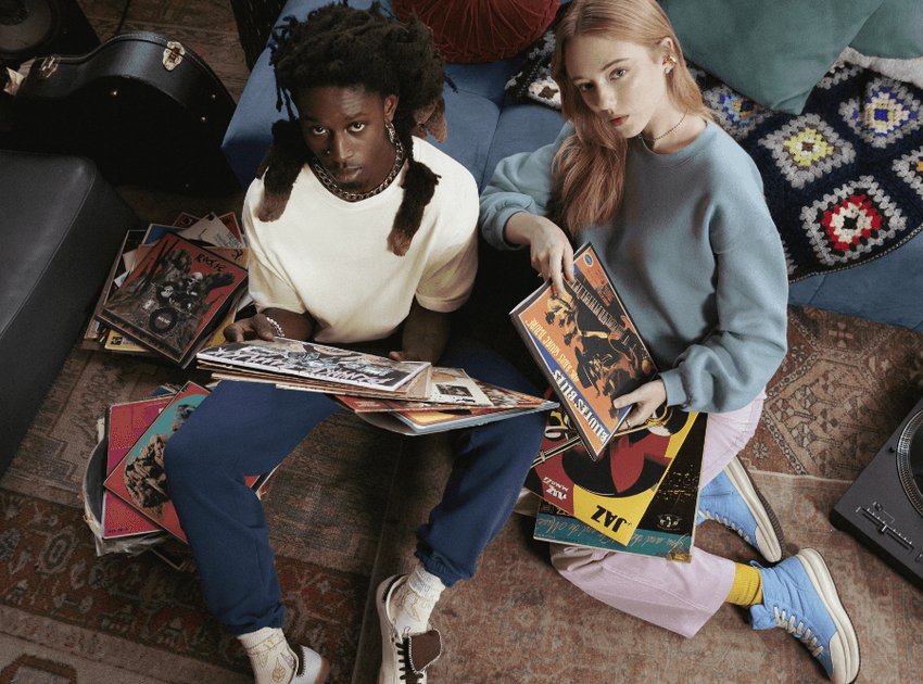 Un homme et une femme sont assis par terre et regardent la caméra en tenant des disques vinyles.