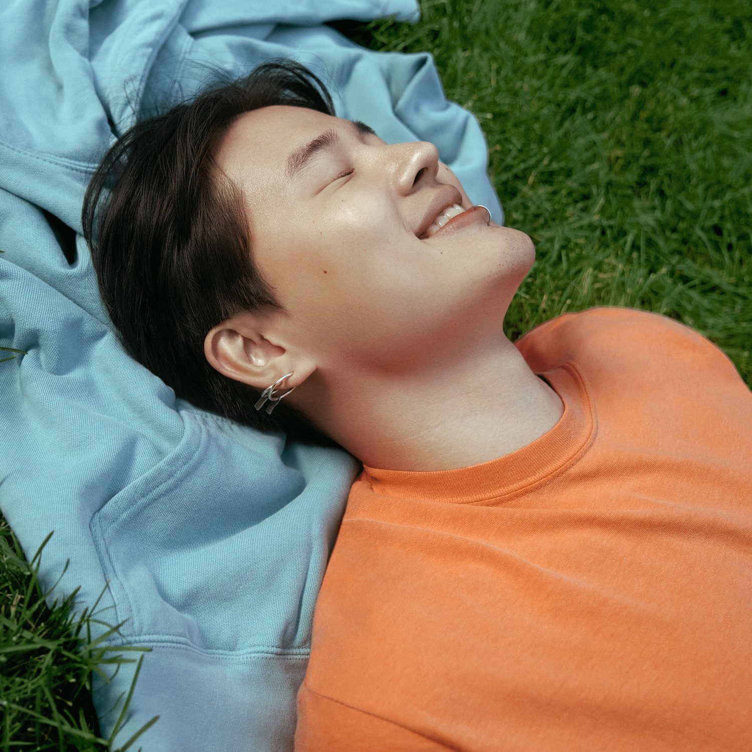 Une personne portant un t-shirt Comfort Colors orange sur l'herbe, fermant les yeux et souriant au soleil.