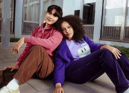 Une femme vêtue de violet et un homme vêtu de rose sont assis par terre et s'appuient l'un sur l'autre.