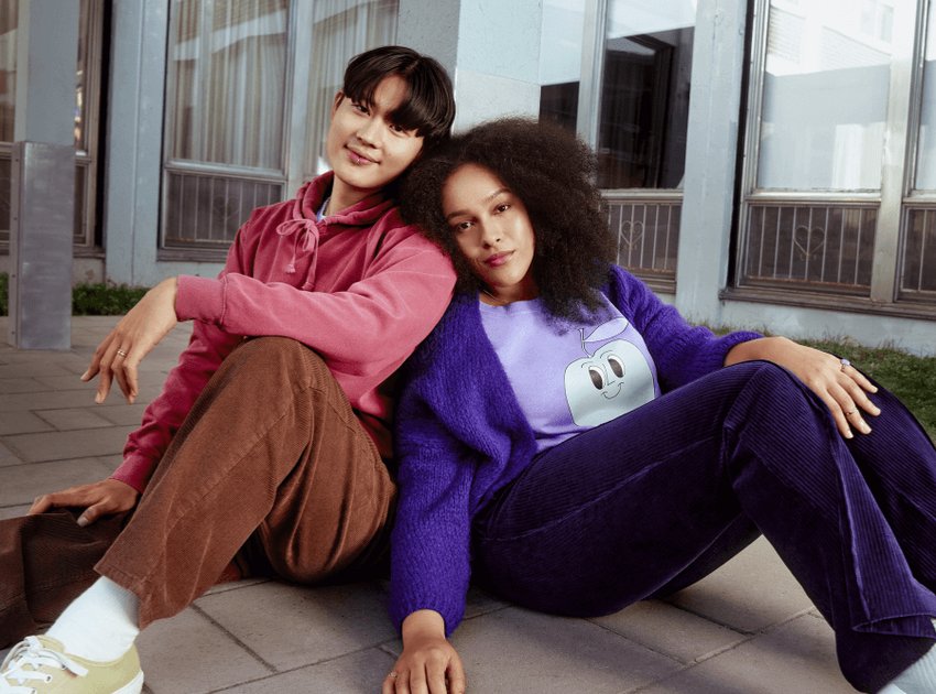 Une femme vêtue de violet et un homme vêtu de rose sont assis par terre et s'appuient l'un sur l'autre.