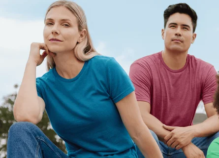 Une femme assise sur des gradins à l'extérieur, vêtue d'une chemise bleue et d'un jean, sourit.