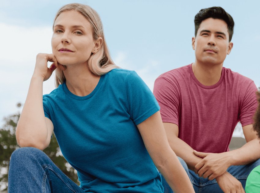Une femme assise sur des gradins à l'extérieur, vêtue d'une chemise bleue et d'un jean, sourit.