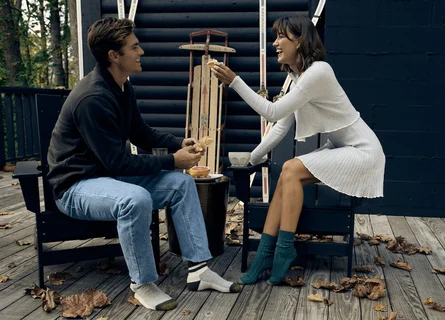 Une femme qui rit, assise à l'extérieur sur une chaise et portant des chaussettes bleues GOLDTOE.
