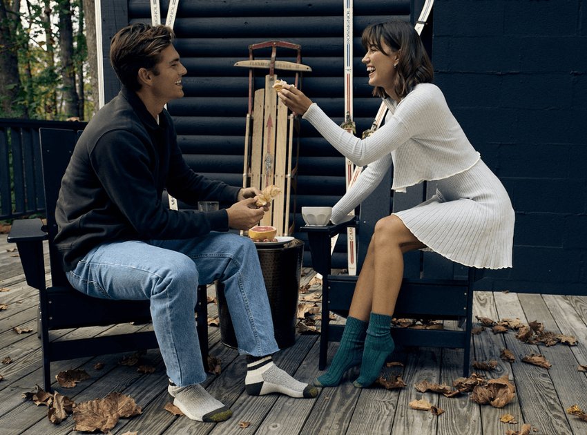 Une femme qui rit, assise à l'extérieur sur une chaise et portant des chaussettes bleues GOLDTOE.