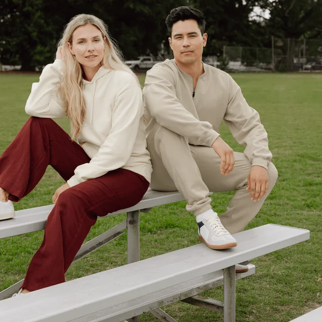 A woman and man are wearing Gildan shirts and pants sitting outside on the bleachers