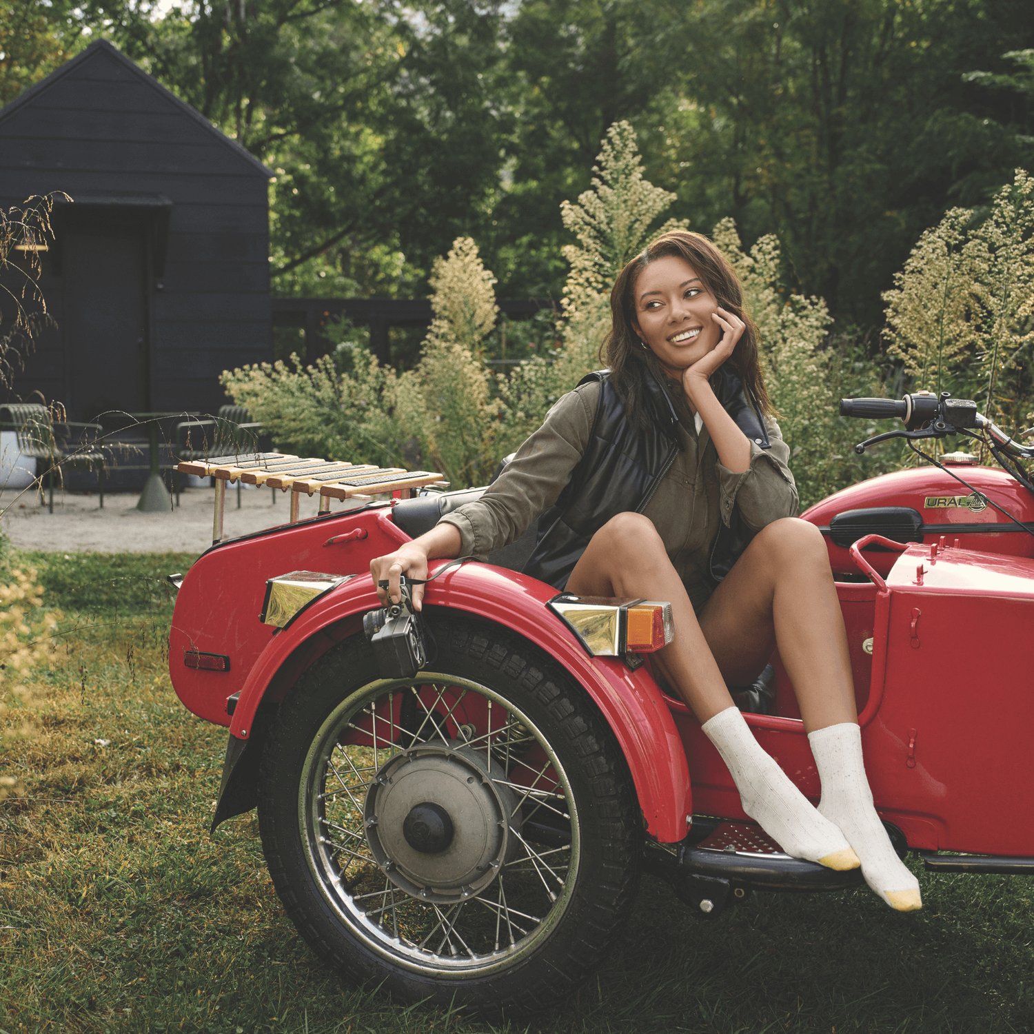 Une femme assise dans une voiture rouge à l'extérieur porte des chaussettes GOLDTOE blanches avec une pointe dorée.