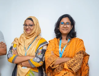 Deux femmes du Bangladesh sourient à la caméra et croisent les bras.