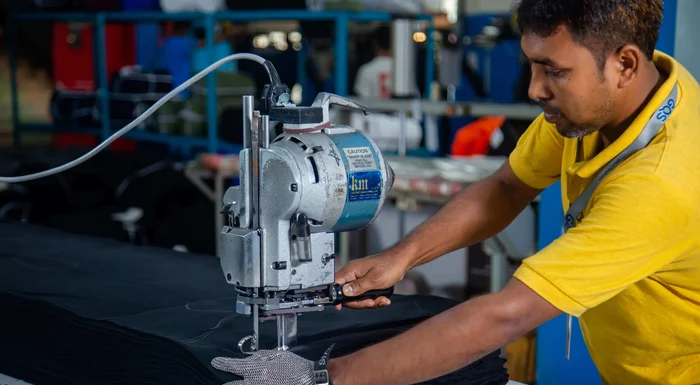 Un homme vêtu d'une chemise jaune utilise une machine à découper le tissu.