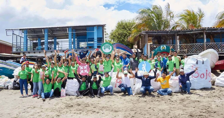 Un grand groupe d’employés au Nicaragua sourient sur la plage, les mains en l’air.