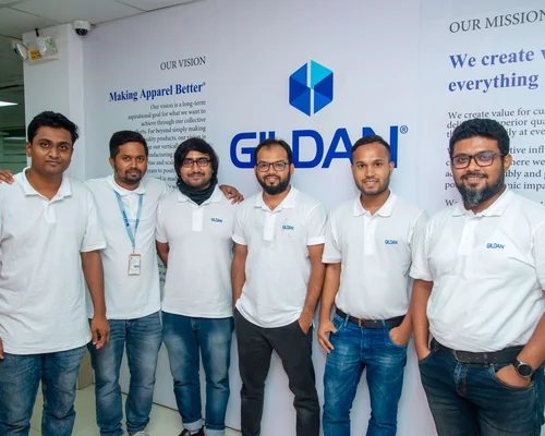 Un grupo de empleados de Bangladesh está de pie junto a una pared en la que hay un cartel de Gildan.