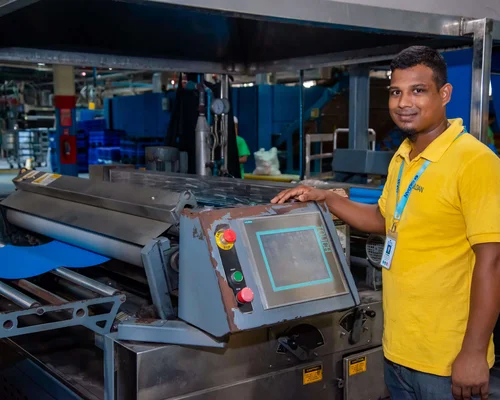 Un homme vêtu de jaune se tient à côté d'une machine et sourit.