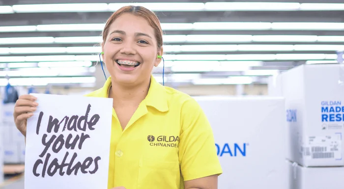 Mariela está sonriendo y sosteniendo un cartel que dice “Hice tu ropa” en español.