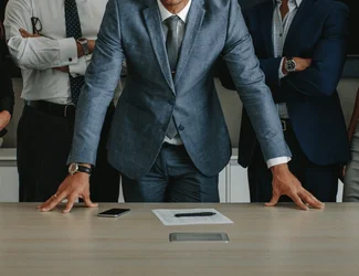 Trois hommes font face à la caméra, les bras croisés, appuyés sur un bureau.