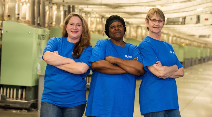 Trois employés de Gildan croisent les bras et sourient dans l'usine de filature.