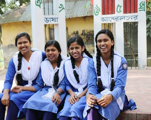 Quatre jeunes femmes au Bangladesh rient en portant un uniforme bleu et des foulards blancs.