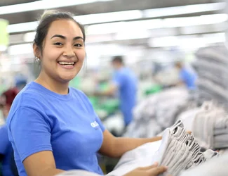 Un employé de couture portant un masque et des lunettes de sécurité utilise une machine à coudre.