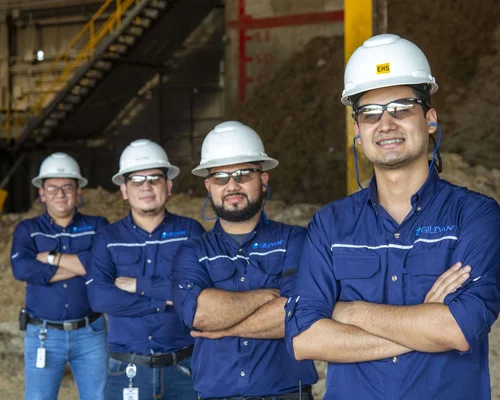 Quatre employés masculins portant des chemises Gildan et des casques de protection sourient.