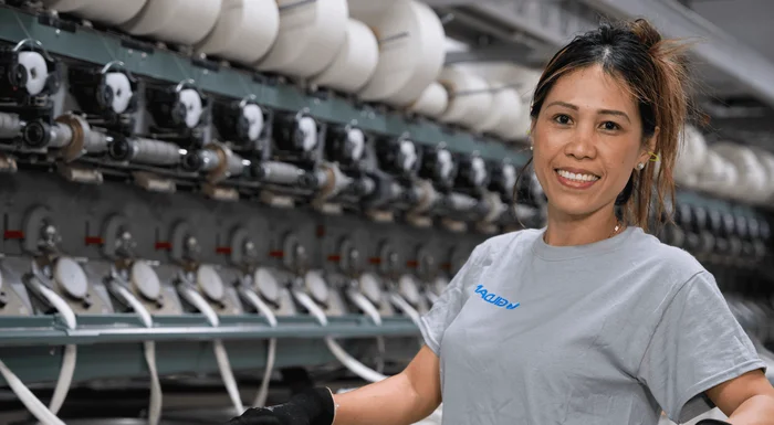 Une femme se tient près des machines à filer et sourit.